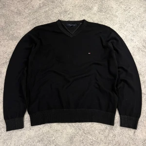 Svart tröja från Tommy Hilfiger - Säljer en stilren svart tröja från Tommy Hilfiger med v-ringning och diskret logga på bröstet. Tröjan har långa ärmar och ribbade muddar vid ärmslut och nederkant. Perfekt för en klassisk look.