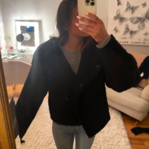 Svart teddyjacka - Mysig svart teddyjacka med en oversized passform. Perfekt för kyliga dagar med sin fluffiga och varma design. Jackan har långa ärmar och stängs med knappar framtill.