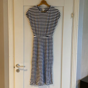 Randig klänning från H&M - Säljer en randig klänning från H&M i storlek XS. Klänningen har ett klassiskt blått och vitt randigt mönster och korta ärmar. Perfekt för en avslappnad stil. Tillverkad i ett mjukt och bekvämt material.