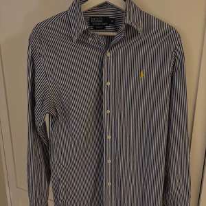 Randig skjorta från Ralph Lauren - Snygg blå och vit randig skjorta från Ralph Lauren i slim fit. Skjortan har långa ärmar och knappar framtill. Perfekt för en stilren look.