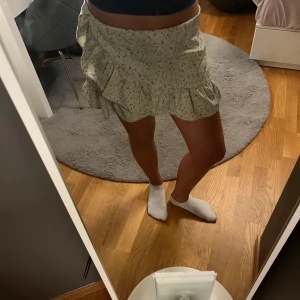 Blommig volangkjol - Söt kortkjol med blommigt mönster och volangdetaljer. Perfekt för varma dagar och ger en romantisk touch till din outfit. Elastisk midja för bekväm passform.