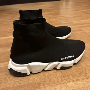  Balenciagas - Snygga svarta sneakers från Balenciaga med en strumpliknande design och vit sula. Skorna har en modern och stilren look med Balenciaga-loggan på sidan och hälen. Perfekta för en trendig och bekväm stil. Storlek 43, hör av er vid frågor 