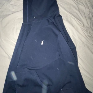 Mörkblå hoodie från Ralph Lauren - Säljer en stilren mörkblå hoodie från Ralph Lauren med dragkedja och det klassiska logotypbroderiet på bröstet. Tröjan har en bekväm passform med långa ärmar och en praktisk känguruficka framtill. Perfekt för en avslappnad look. Köpt från rl i stockholm använt hyfsat mycket i storlek M inga hål eller märken.