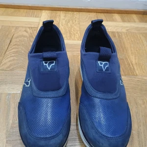Blå sneakers med vit sula - Snygga blå sneakers med en stilren design och vit sula. Skorna har en elastisk detalj för enkel på- och avtagning. Perfekta för en avslappnad stil.