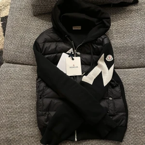 Moncler Cardigan - Säljer min Moncler cardigan då den inte riktigt var min grej. Snygg stilren look med M loggan över armen och perfekt tjocklek nu till våren. Köptes på Plick så kan ej garantera äkthet men NFC och QR kod fungerar utan problem. Moncler dustbag och lapparna på bild 1 fås med!✅ 