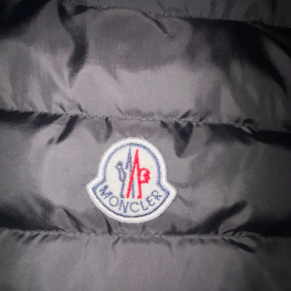 Snygg svart dunväst från Moncler med dragkedja och broderad logotyp på bröstet. Perfekt för kyligare dagar och kalla sommardagar.. Takit.