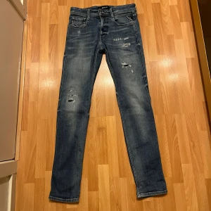 Blå jeans från Replay - Snygga blå jeans från Replay med slitna detaljer och en klassisk femficksdesign. Tillverkade i hållbar bomull för en bekväm passform. Perfekta för en avslappnad stil.
