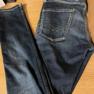 Mörkblå jeans från Replay - Snygga mörkblå jeans från Replay med klassisk femficksdesign och kontrastsömmar. Jeansen har en knappgylf och är i modellen Anbass, vilket ger en modern och stilren look.