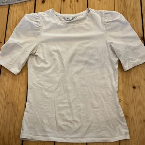 Vit topp från ONLY - Säljer en stilren vit topp från ONLY i storlek XS. Toppen har korta puffärmar och en rund halsringning, perfekt för en enkel och klassisk look. Materialet känns mjukt och bekvämt mot huden.