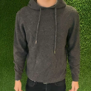 Mörkgrå  100% Merino-Ull Hoodie - Säljer en stilren mörkgrå hoodie med justerbara snören i huvan. Perfekt för en avslappnad look. Tröjan har långa ärmar och en mjuk känsla.