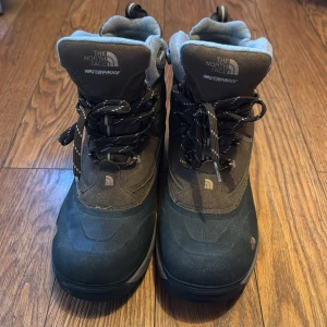 Vattentäta kängor från The North Face - Säljer ett par robusta och vattentäta kängor från The North Face. De är bruna med svarta detaljer och har snörning framtill. Perfekta för kalla och blöta dagar med bra isolering för extra värme.