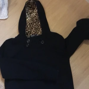 Svart hoodie med leopardmönstrad huva - Säljer en svart hoodie från BFDI med en cool leopardmönstrad insida i huvan. Tröjan har knappar framtill och är perfekt för en avslappnad stil. Passar bra till jeans eller leggings. 🐆