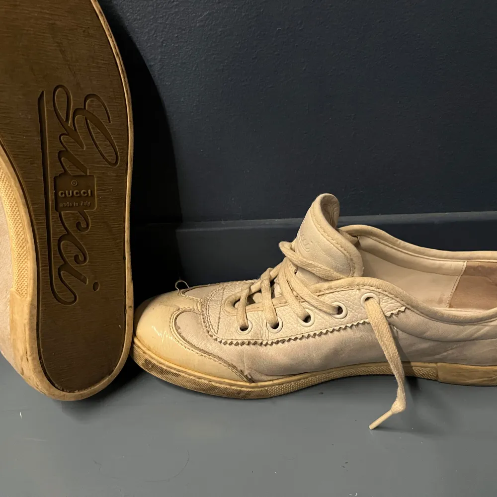Snygga beige sneakers från Gucci med klassiska ränder i grönt och rött på sidan. Skorna har snörning och är tillverkade i skinn. Perfekta för en stilren look.lite smutsiga men väldigt snygga.. Kengät.