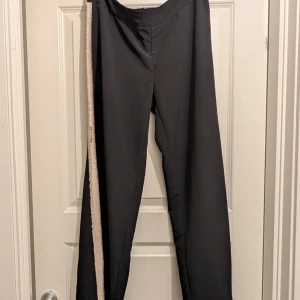 Svarta byxor med glittrig  paljett detalj - Snygga svarta byxor med en glittrig rand längs sidan. Perfekta för att ge en extra touch till din outfit. Byxorna har en rak passform och är tillverkade i ett bekvämt material. Storlek 38/40
