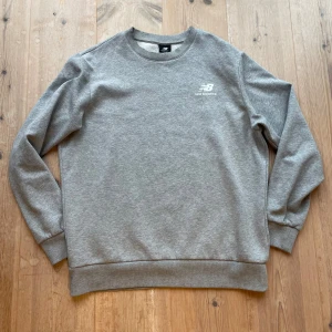 Grå sweatshirt från New Balance - Säljer en stilren grå sweatshirt från New Balance. Tröjan har en klassisk rund halsringning och långa ärmar. Den är tillverkad i ett mjukt material. Hör av dig vid frågor!