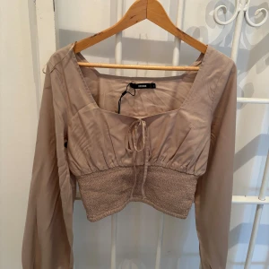 Beige långärmad topp från Bershka - Säljer en beige långärmad topp från Bershka. Toppen har en knytning framtill och en croppad design med ribbad nederdel. 