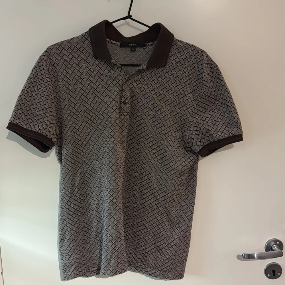Säljer en stilren pikétröja från Gucci med ett diskret mönster i beige och brunt. Tröjan har korta ärmar och en klassisk krage med knappar framtill. Perfekt för en avslappnad men ändå elegant look. (M) sitter som en s för att den är slimfit . Neuletakit & Villapaidat.