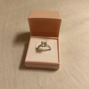 Silverring med sten  - Elegant silverring 925 med en klar sten i mitten. Ringen kommer i en stilren rosa ask med Amor logotypen på locket. Perfekt för speciella tillfällen eller som en fin gåva.