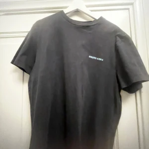 Svart t-shirt med tryck från Axel Arigato - Snygg svart t-shirt från Axel Arigato med tryck i turkos på både fram- och baksida. Perfekt för en avslappnad stil. Passar S