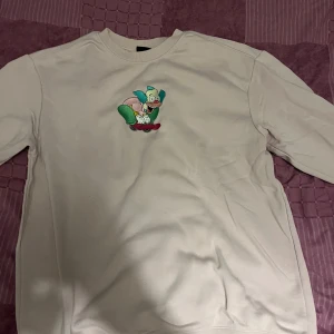 Rosa sweatshirt med tecknad figur - Säljer en ljus rosa sweatshirt med en färgglad tecknad figur på framsidan. Tröjan har långa ärmar och en rund halsringning. Perfekt för en avslappnad stil. Använd max 5 gånger. 