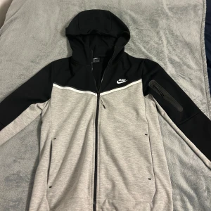 Grå och svart huvtröja från Nike - Säljer en grå och svart huvtröja från Nike med dragkedja och huva. Nästan aldrig använd pga för liten storlek, inga fel på den.