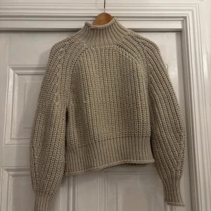 Beige stickad tröja från H&M - Säljer en mysig beige stickad tröja från H&M. Tröjan har en hög krage och långa ärmar med ribbade muddar. Perfekt för kyliga dagar!
