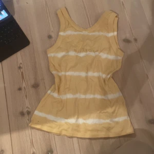 Gul och vit randig linnetopp från Billabong - Säljer en somrig gul och vit randig linnetopp från Billabong. Toppen är ärmlös och har en bekväm passform, perfekt för varma dagar. Den har ett tryck med Billabong-loggan på framsidan.