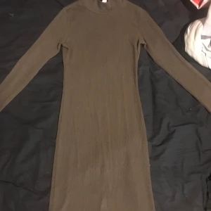 Brun ribbad klänning från Kikiriki - Säljer en stilren brun ribbad klänning från Kikiriki i storlek XS. Klänningen har långa ärmar och en enkel design som passar perfekt för höst och vinter. Perfekt för dig som gillar en minimalistisk stil.