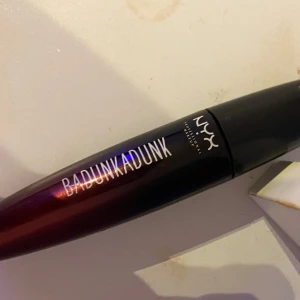 Mascara från NYX - Snygg mascara från NYX med namnet 'Badunkadunk'. Den har en svart hylsa med en röd toning och en borste som ger volym till fransarna. Perfekt för att framhäva ögonen med en dramatisk look.