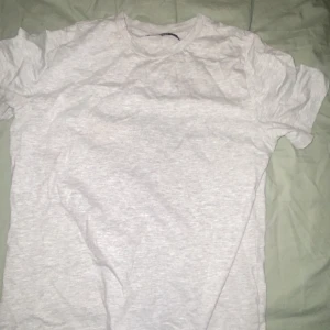 Grå t-shirt - Säljer en klassisk grå t-shirt i bomull. Perfekt basplagg för alla tillfällen. T-shirten har en normal passform och korta ärmar.