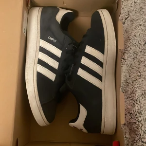Mörklbåa Adidas Campus sneakers - Snygga mörkblå Adidas Campus sneakers med vita ränder och snörning. Perfekta för en avslappnad stil.