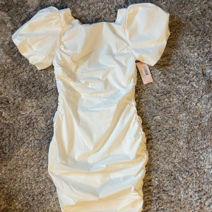 Vit klänning från Nelly - Säljer en snygg vit klänning från Nelly med puffiga kortärmar och rynkade detaljer längs sidorna. Klänningen är figursydd och är perfekt till studenten. 