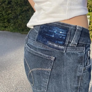 Mörkblå jeans från Calvin Klein - Snygga mörkblå jeans från Calvin Klein med paljett-detalj på baksidan. Köpta här på plick men har själv aldrig använt bilderna är från hon jag köpte de av. Skriv för mått och egna bilder💗finns en fläck på baksidan men den syns knappt och vet ej om d går bort i tvätten 