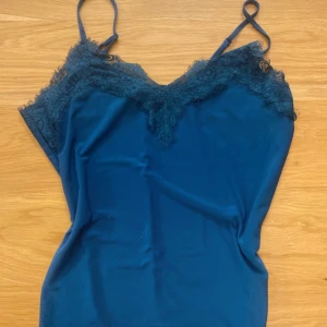 Mörkblå linne med spetsdetaljer - Snygg mörkblå linne med smala axelband och vacker spetsdetalj längs urringningen. Perfekt för en stilren och elegant look.
