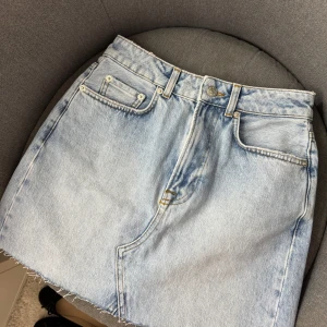 Ljusblå jeanskjol - Kjolen har en knapp och dragkedja framtill. Köpt på sellpy men från NA-KD
