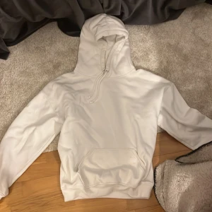 Vit hoodie från bikbok - Säljer en stilren vit hoodie med en stor ficka framtill och justerbar huva. Perfekt för en avslappnad look. Passar bra till både jeans och mjukisbyxor.