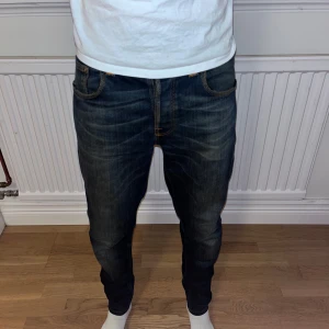 Blå jeans från Nudie Jeans - Snygga blå jeans från Nudie Jeans med oranga sömmar. Jeansen har en straight/slim passform och är tillverkade i slitstarkt denim. Perfekta för grisch stilen. De är i W31/L32. 
