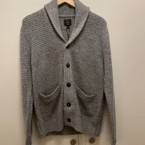 Grå stickad kofta från Next - Säljer en stilren grå stickad kofta från Next med knappar framtill och två praktiska fickor. Perfekt för kyliga dagar med sin mjuka och varma känsla. Koftan har en klassisk krage och långa ärmar. Köpte för 780 mitt pris 700 helt oanvänd 