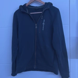 Mörkblå zip hoodie  från Sail Racing - Snygg svart jacka från Sail Racing med dragkedja och huva. Perfekt för en casual look. Jackan har en stilren design med Sail Racing-logga på bröstet och huvan. Den är jätte fin för hösten och bra att style 