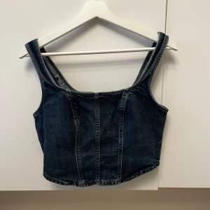Mörkblå jeanskorsett - Snygg mörkblå jeanskorsett med dragkedja fram. Den har breda axelband och en croppad passform som ger en cool look. Perfekt för att styla med olika outfits.