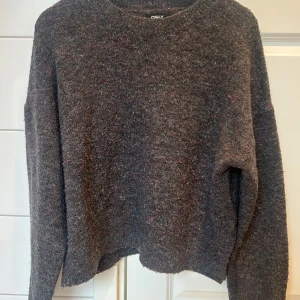 Gråmelerad tröja från ONLY - Säljer en mysig gråmelerad tröja från ONLY med färgglada små detaljer. Tröjan har långa ärmar och en rund halsringning. Sitter väldigt snyggt o har en slit ner till. Färgerna i tröjan syns inte allt för väl från långt håll tycker jag, men det är en otroligt fin detalj. Storlek L men skulle mer säga att det är en M och sitter oversized som S