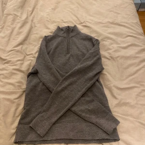 Grå merinoulltröja från These Glory Days - Säljer en stilren grå tröja i merinoull från These Glory Days. Tröjan har en halv dragkedja och långa ärmar, perfekt för kyligare dagar. Den är mjuk och bekväm med en klassisk design. Bara använd 4 gånger! Ny pris 1100!