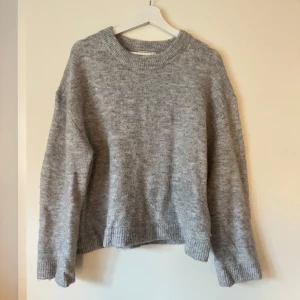 Grå stickad tröja från H&M - Mysig grå stickad tröja från Ginatricot med rund hals och långa ärmar. Perfekt för kyliga dagar med sin mjuka och bekväma passform. Ribbstickade muddar vid ärmslut och nederkant ger en klassisk look.