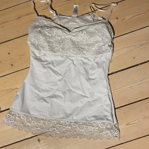 Två linnen med spetsdetaljer - Säljer två eleganta linnen med spetsdetaljer. Ett i vitt och ett i svart, båda med vacker spets upptill och nedtill. Perfekta för en stilren look.