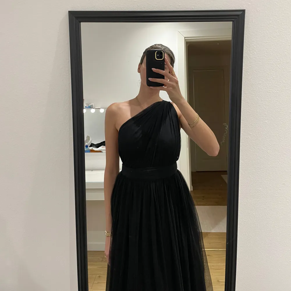 Elegant svart långklänning med oneshoulder-design och öppen rygg. Perfekt för formella tillfällen med sin flytande siluett och stilrena look.. Mekot.