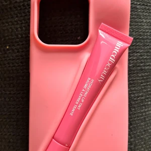 Trendigt rosa mobilskal med lipgloss! - Trendigt rosa mobilskal i silikon som passar IPhone 13/14/15 och deras PRO-modeller. Ett rosa hydrating liptint från Tinted Beauty medföljer. Nytt och oanvänt. 