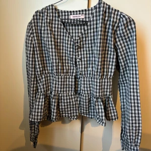 Peplumblus i rutigt tyg - Fin blus i rutigt typ med volang nedtill och knappar framtill. Jätte gullig passform. Säljer pga för liten. Storlek XS/S. 
