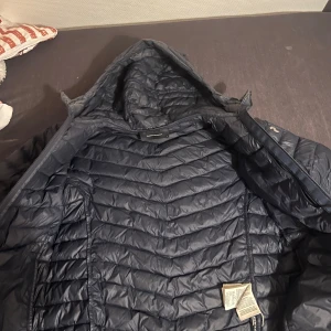 Mörkblå dunjacka från Peak Performance - Säljer en mörkblå dunjacka från Peak Performance med huva och dragkedja. Jackan är quiltad och tillverkad i Pertex-material, vilket gör den både lätt och varm. Perfekt för kyliga dagar. Har inte använt den mycket ordentliga priset är 3000kr 