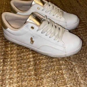  GULD GLITTER SNEAKERS Polo Ralph Lauren - Snygga vita sneakers från Polo Ralph Lauren med gyllene detaljer och logotyp. Skorna har snörning och en glittrig häl i guld. Perfekta för en stilren look, våren och sommaren! Har använt de cirka 3 gånger.🩷