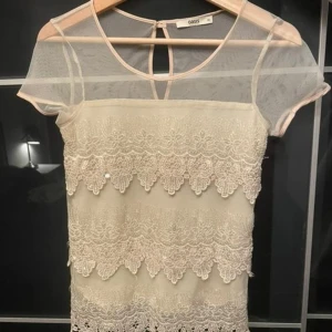 Vit spetsblus från Oasis - Elegant vit blus från Oasis med spetsdetaljer och korta ärmar. Blusen har en transparent övre del och en fin spetskant längst ner. 
